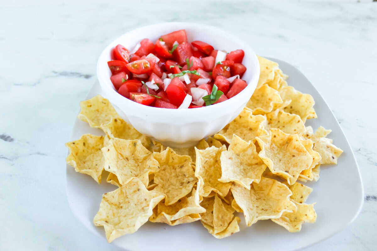 Fresh watermelon salsa with tomatoes, onion, and basil, surrounded by tortilla chips.