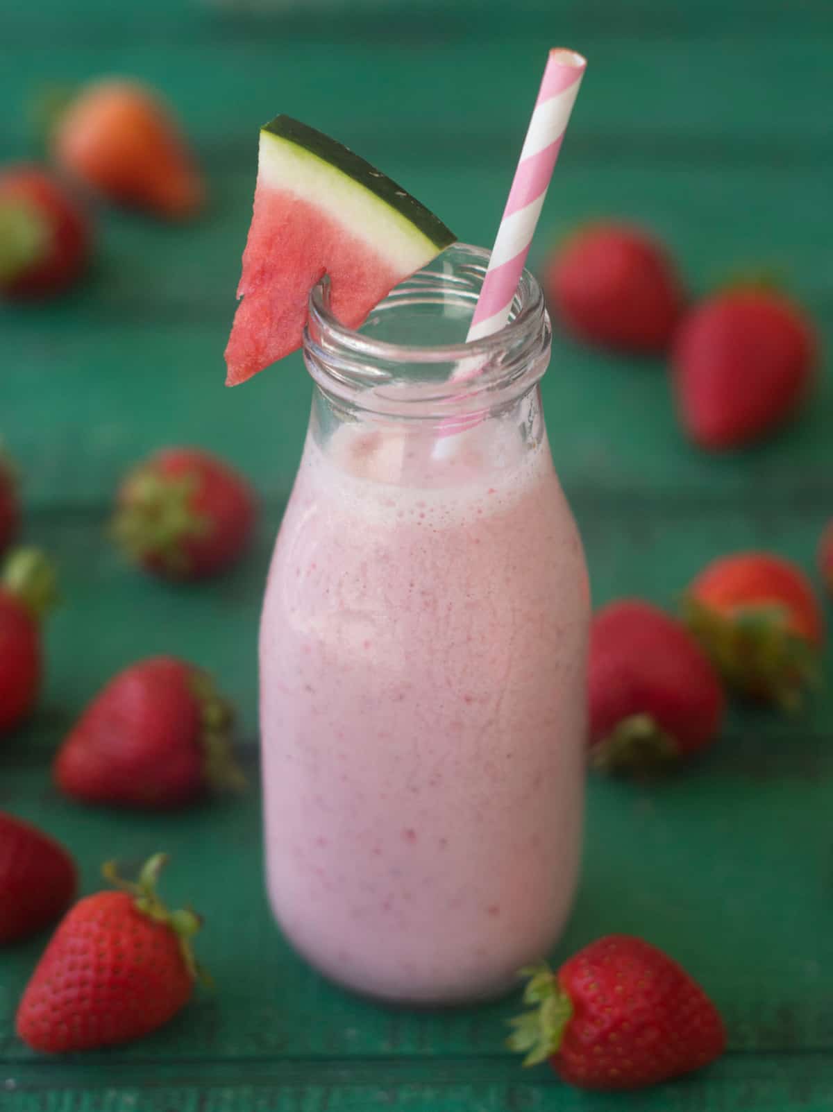 Fruit smoothie in jar with pink straw and watermelon wedge.