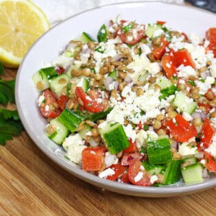 Lentil salad in a whole bowl with lemon and parsley in background.